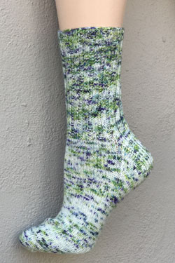 A speckled sock in shades of blue and green with a light green background on a foot form